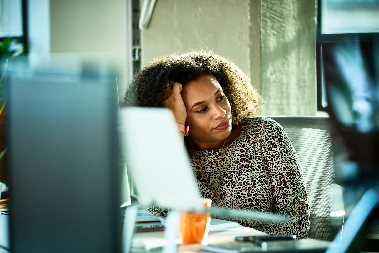 A woman sitting at a desk surrounded by computers, had her head in her hand.
