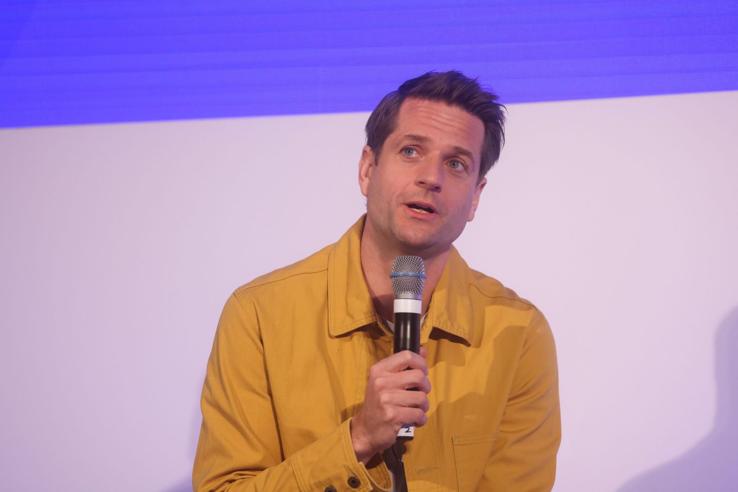 Sebastian Siemiatkowski, wearing a yellow shirt, talks into a microphone.