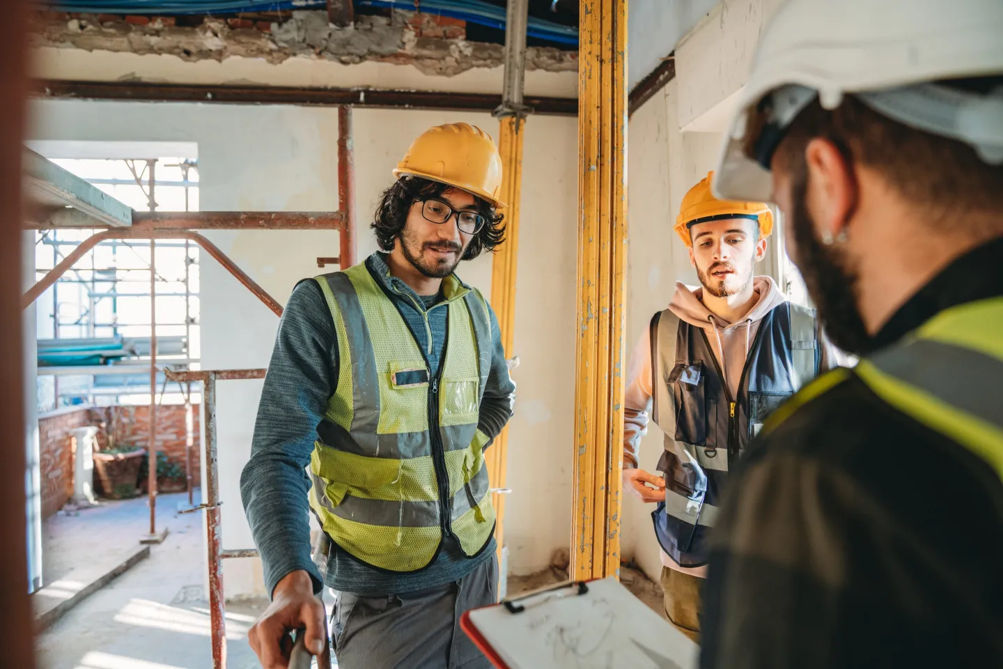 Man with clipboard explains construction project to two young adults.