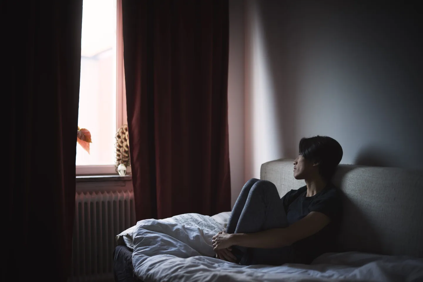 Young man sitting alone, looking forlorn, in a darkened room