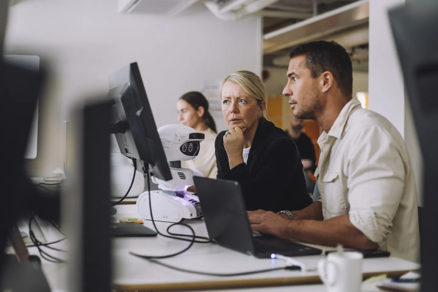 A professional woman at a desk helping train a another worker to use technology.