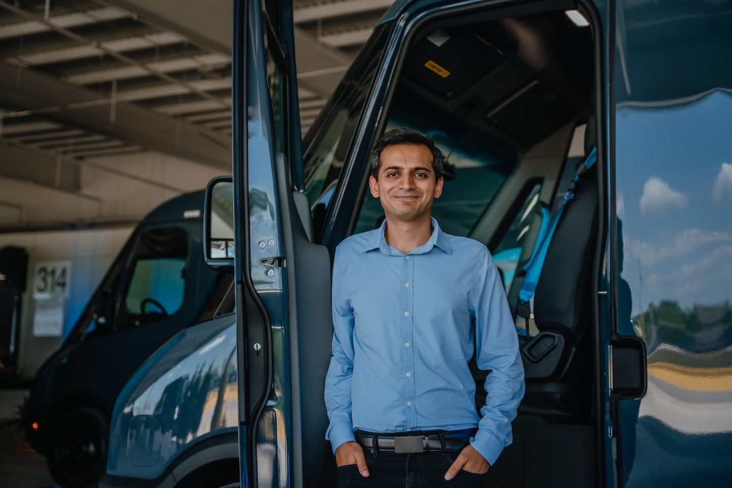 Udit Madan stands in front of an open driver side door of a Rivian delivery van.